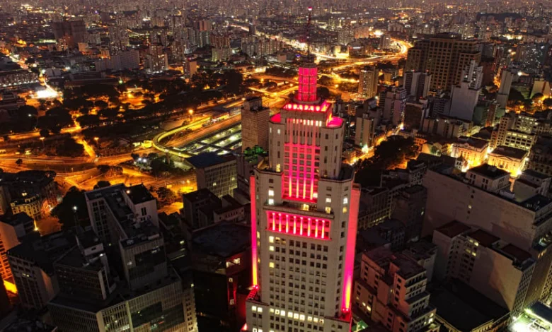 a cityscape with a tall building with red lights